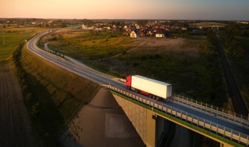 Hva er HVO100 - luftfoto av en lastebil som kj&oslash;rer p&aring; en landevei i solnedgangen, med en by og en bro i et nordisk landskap &ndash; et symbol p&aring; en vognpark som kj&oslash;rer p&aring; fornybar diesel