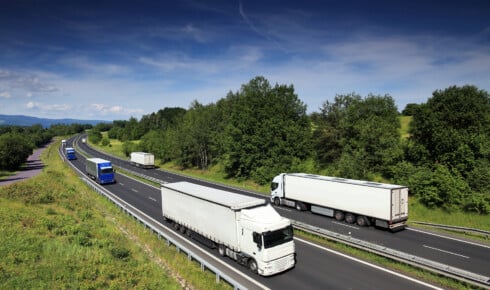 Klimaregler i transport - flere lastebiler kj&oslash;rer p&aring; en flerfelts motorvei gjennom gr&oslash;nt kupert landskap &ndash; et bilde p&aring; den veitransporten som omfattes av EUs klima- og utslippsregler